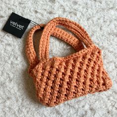 an orange crocheted purse sitting on top of a white carpet next to a black tag