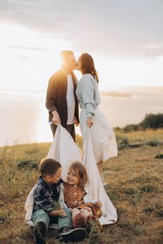 three children sitting on the ground in front of an adult and one child kissing each other