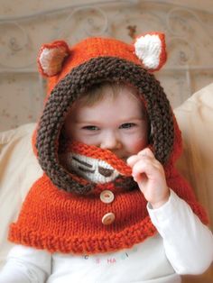 a young child wearing a knitted hat and scarf with fox ears on it's head