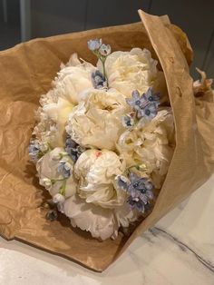 a bouquet of white and blue flowers in a brown paper bag on a counter top