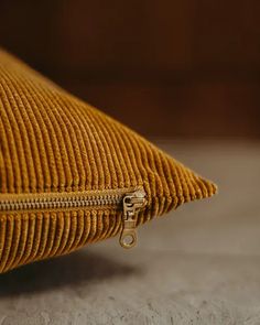 a close up of a yellow corded pillow on the floor with a gold zipper