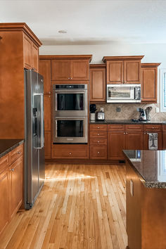 a large kitchen with wooden floors and stainless steel appliances in the cabinets, along with an island