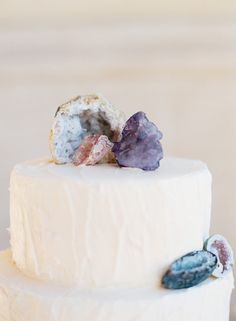 a three layer cake with white frosting and colorful rocks on top