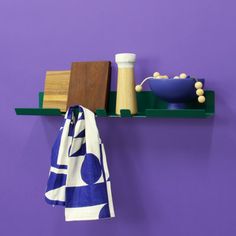 a towel hanging on a purple wall next to a bowl and wooden block with beads