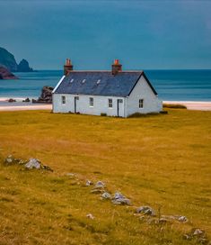 a small white house sitting on top of a lush green field next to the ocean