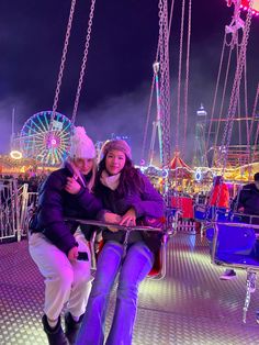 two women are sitting on a swing at the carnival with ferris wheel in the background