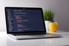 an open laptop computer sitting on top of a white desk next to a potted plant