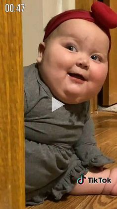 a baby is sitting on the floor wearing a red headband and smiling at the camera