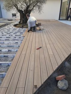 a man kneeling down on top of a wooden deck next to a tree and rocks