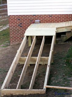 an unfinished deck being built in front of a brick building with grass and dirt around it