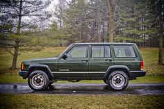 a green jeep parked on the side of a road in front of trees and grass