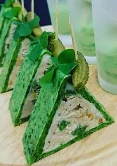 four pieces of food with green toppings on a cutting board next to glasses and water