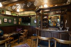 the interior of a bar with wooden tables and stools, green wallpaper and wood paneling