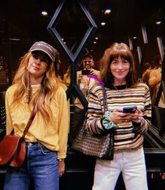 two women standing next to each other holding cell phones