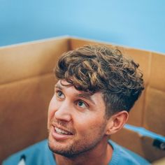 a young man with curly hair sitting in a chair looking up at the camera and smiling