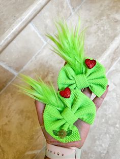 a hand holding two green hair bows with strawberries on them and one red strawberry in the middle