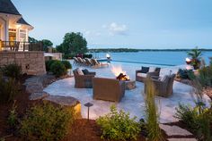 an outdoor fire pit surrounded by chairs and tables next to the ocean at night time