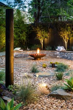 a fire pit in the middle of a garden surrounded by rocks and trees with lights on it