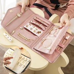 a woman sitting at a table holding a pink purse filled with jewelry and other items