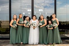 a group of women standing next to each other in front of a glass building holding bouquets