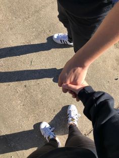 two people holding hands while standing on concrete