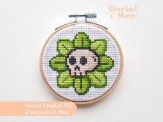 a cross stitch pattern with a skull in the center and leaves on it, hanging from a hoop