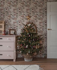 a small christmas tree sitting in the corner of a room next to a dresser and door