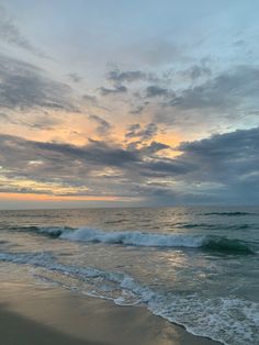 the ocean waves come in to shore as the sun goes down over the horizon and clouds loom overhead