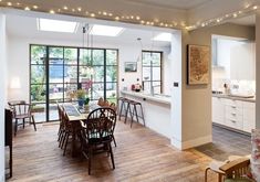 an open kitchen and dining room with wooden floors, white walls and ceiling lights are lit by string lights