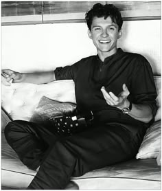 a black and white photo of a man sitting on a couch with his hands in the air