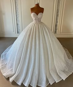 a white ball gown on a mannequin stand in front of a wall and floor