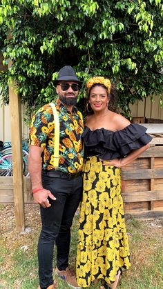 a man and woman standing next to each other in front of a tree with yellow flowers on it