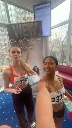 two young women standing next to each other in front of a poster