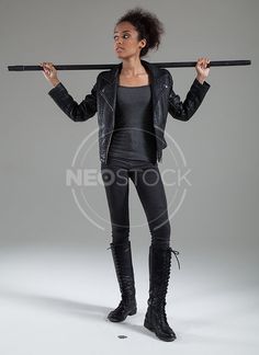 a woman in black leather clothes holding a pole over her head and looking at the camera