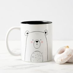 a white and black coffee mug with a donut on the side next to it