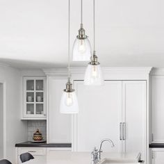 a kitchen with white cabinets and an island in front of the countertop is lit by three pendant lights