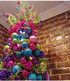 a colorful christmas tree with ornaments on it in front of a brick wall and window