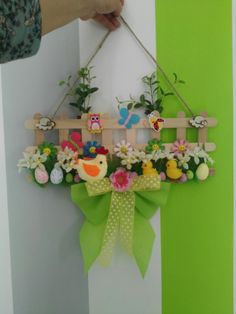 a person holding up a wooden sign with flowers and birds on it, hanging from a green ribbon