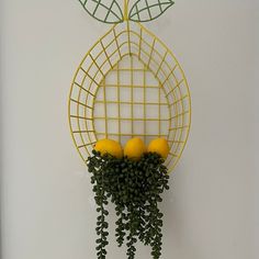 a yellow wire fruit basket with lemons and green leaves hanging from it's sides