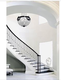 a white staircase with chandelier and bench in the middle of it, leading to an open floor plan