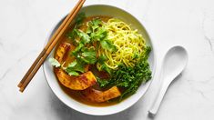 a bowl filled with noodles and vegetables next to chopsticks on a marble surface