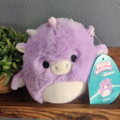 a purple stuffed animal sitting on top of a wooden table next to a green plant