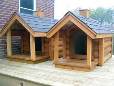 two wooden dog houses sitting on top of a wooden deck next to a brick building