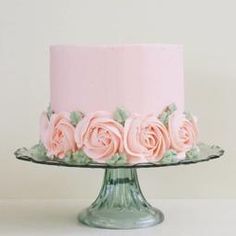 a cake with pink frosting and roses on top is sitting on a glass plate