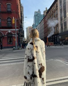 a woman in a fur coat is walking down the street with her hand on her hip