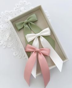 three bow ties in a box on a lace doily next to a white and pink ribbon