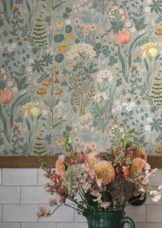 a green vase filled with lots of flowers on top of a tiled counter next to a wall