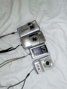 three cameras laying on top of a bed next to each other with cords around them