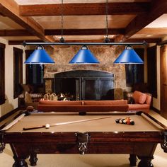 a pool table with two blue lamps hanging from it's ceiling in a living room