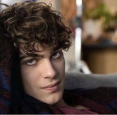 a young man with curly hair and blue eyes is wrapped in a blanket looking at the camera